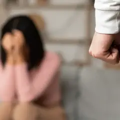 Zaciśnięta pięść na pierwszym planie, w tle kobieta zakrywająca twarz.