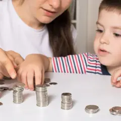 Kobieta i dziecko liczą monety ułożone w stosy na białym stole.