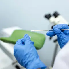Ręce w niebieskich rękawiczkach przygotowują próbkę do badań cytologicznych. Wyniki będą gotowe wkrótce.