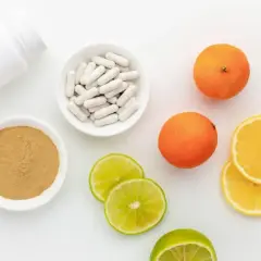 Biała butelka, miseczki z proszkiem i kapsułkami, pomarańcze, cytryny i limonki.