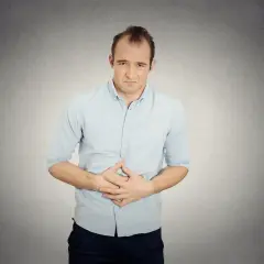 Mężczyzna trzymający się za brzuch z grymasem bólu na twarzy.