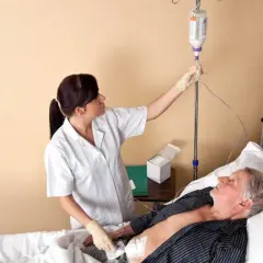 Pielęgniarka podłącza kroplówkę starszemu pacjentowi leżącemu w łóżku.