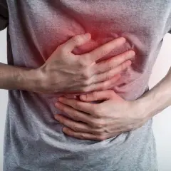 Osoba w szarym t-shircie trzyma się za klatkę piersiową, gdzie widoczny jest czerwony obszar bólu.