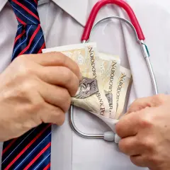 Lekarz w białej koszuli i krawacie wkłada pieniądze do kieszeni, obok stetoskopu.