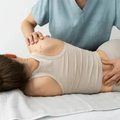 Fizjoterapeuta wykonuje masaż pleców pacjentki leżącej na kozetce.