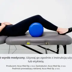Osoba leżąca na kozetce z niebieską piłką pod kolanami.