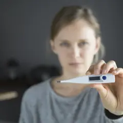 Kobieta trzyma termometr cyfrowy, wskazujący na podwyższoną temperaturę.