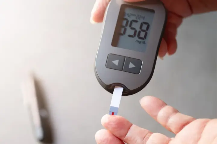 Dłoń z glukometrem i paskiem testowym, na którym widoczny jest wynik 358 mg/dL.