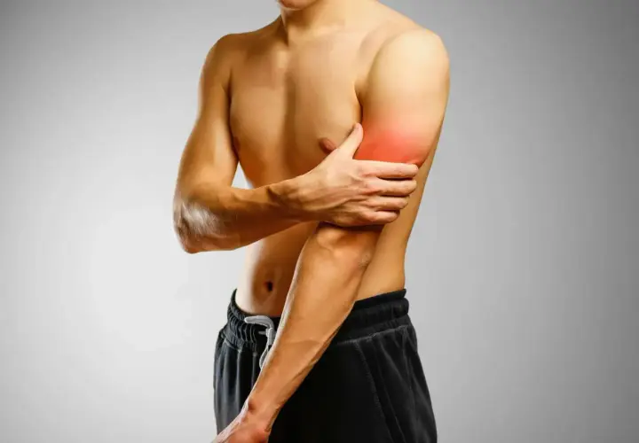 Mężczyzna trzymający się za ramię z zaznaczonym bólem w bicepsie.