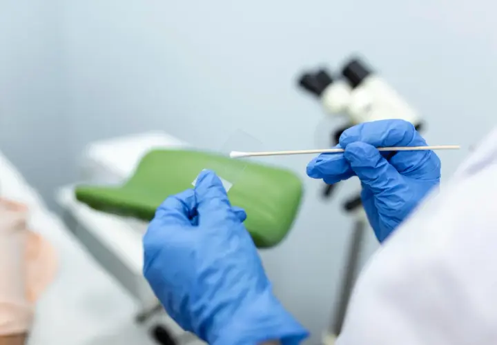 Ręce w niebieskich rękawiczkach przygotowują próbkę do badań cytologicznych. Wyniki będą gotowe wkrótce.