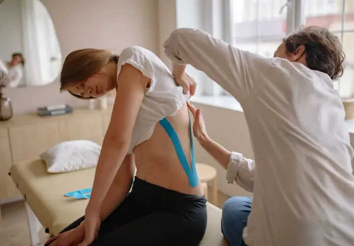 Fizjoterapeuta zakłada taśmę kinezjotaping na plecy pacjentki.
