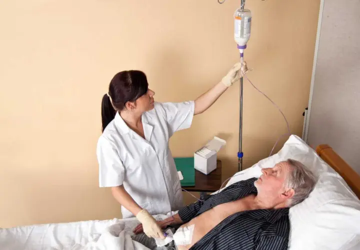 Pielęgniarka podłącza kroplówkę starszemu pacjentowi leżącemu w łóżku.