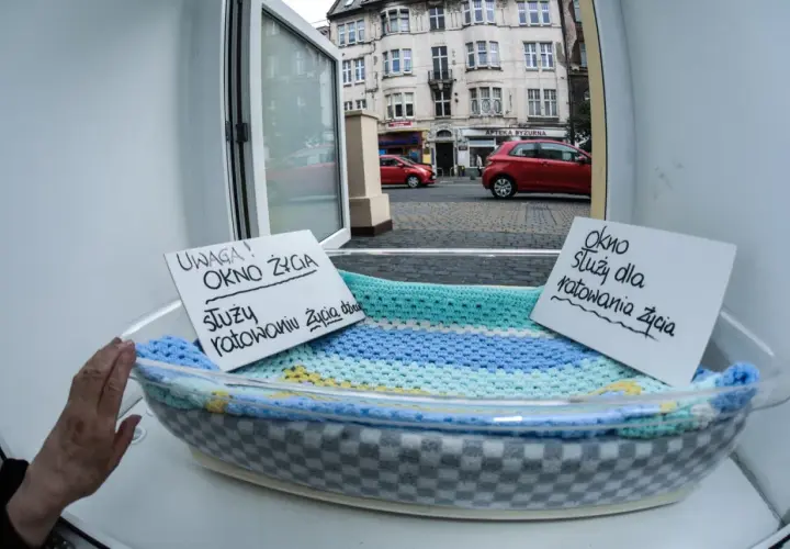 Okno życia z tabliczkami informacyjnymi w koszu, widok na ulicę z budynkami i samochodami.