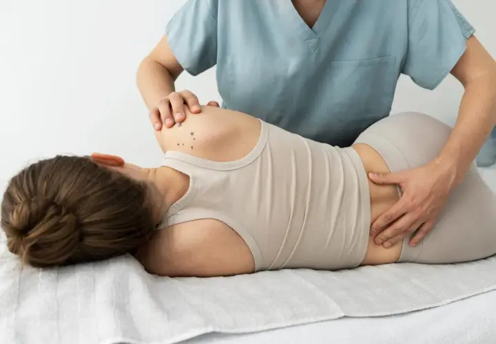 Fizjoterapeuta wykonuje masaż pleców pacjentki leżącej na kozetce.