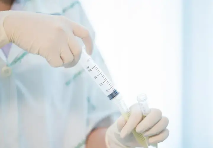 Ręce w rękawiczkach trzymają strzykawkę z płynem i probówkę.