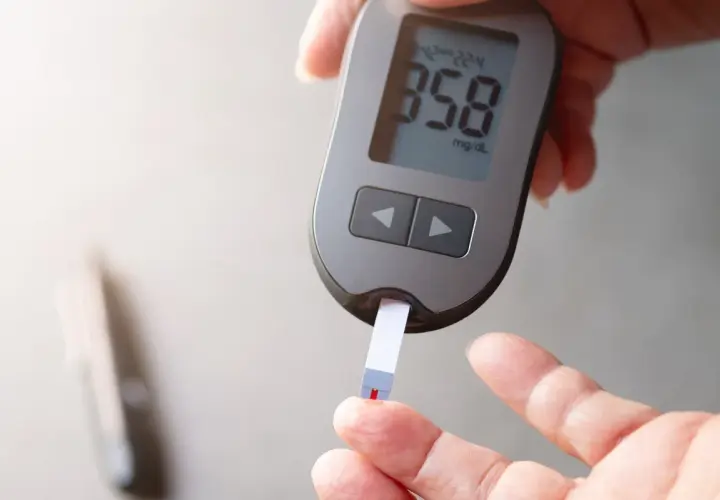 Dłoń z glukometrem i paskiem testowym, na którym widoczny jest wynik 358 mg/dL.