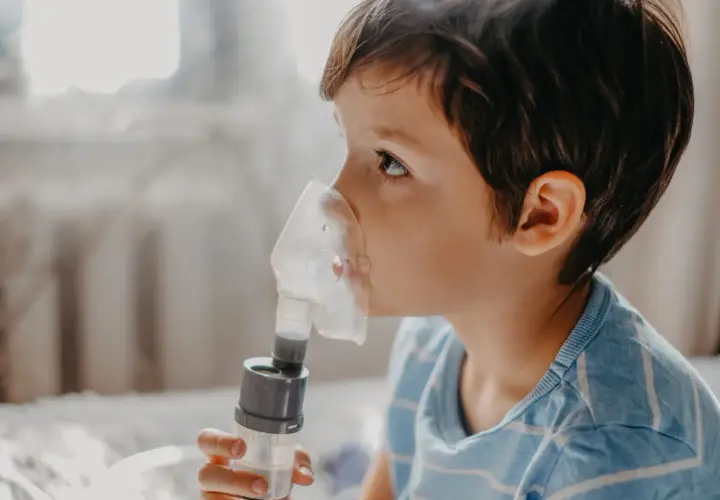 Chłopiec w masce inhalatora wykonuje inhalację solą fizjologiczną.