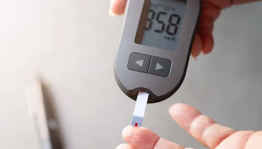 Dłoń z glukometrem i paskiem testowym, na którym widoczny jest wynik 358 mg/dL.