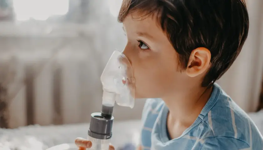 Chłopiec w masce inhalatora wykonuje inhalację solą fizjologiczną.
