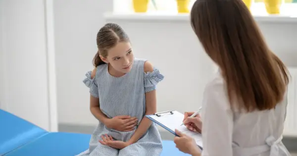 Dziewczynka w niebieskiej sukience trzyma się za brzuch podczas wizyty u lekarza.